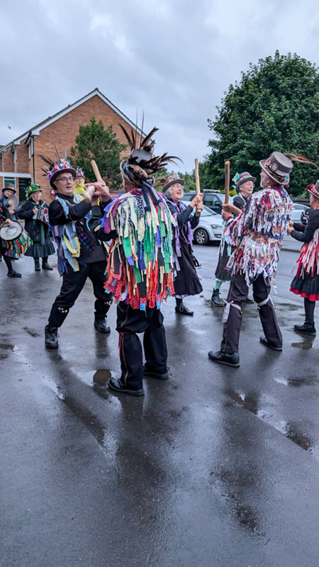 Plum Jerkum Morris dancers in their tatter jackets dancing on a damp surface with many puddles. 