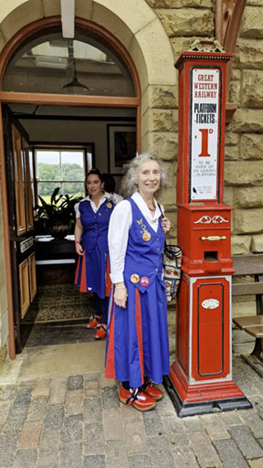 two dancers leaving the victorian decorated waiting room. One stands next to a bright red platform ticket machine.
