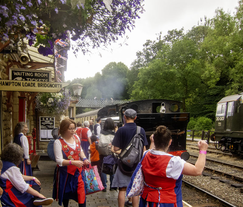 dancers standing on a flower bedecked platform as the steam train arrives