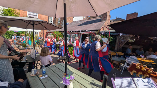 dancers performing in a very confined space in a cafe yard, with musicians and spectators seated at tables around 