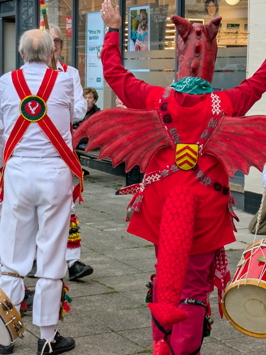 Looking from behind at a White Hart dancer and the Cardiff 'Dragon' dancing side by side in Alcester.